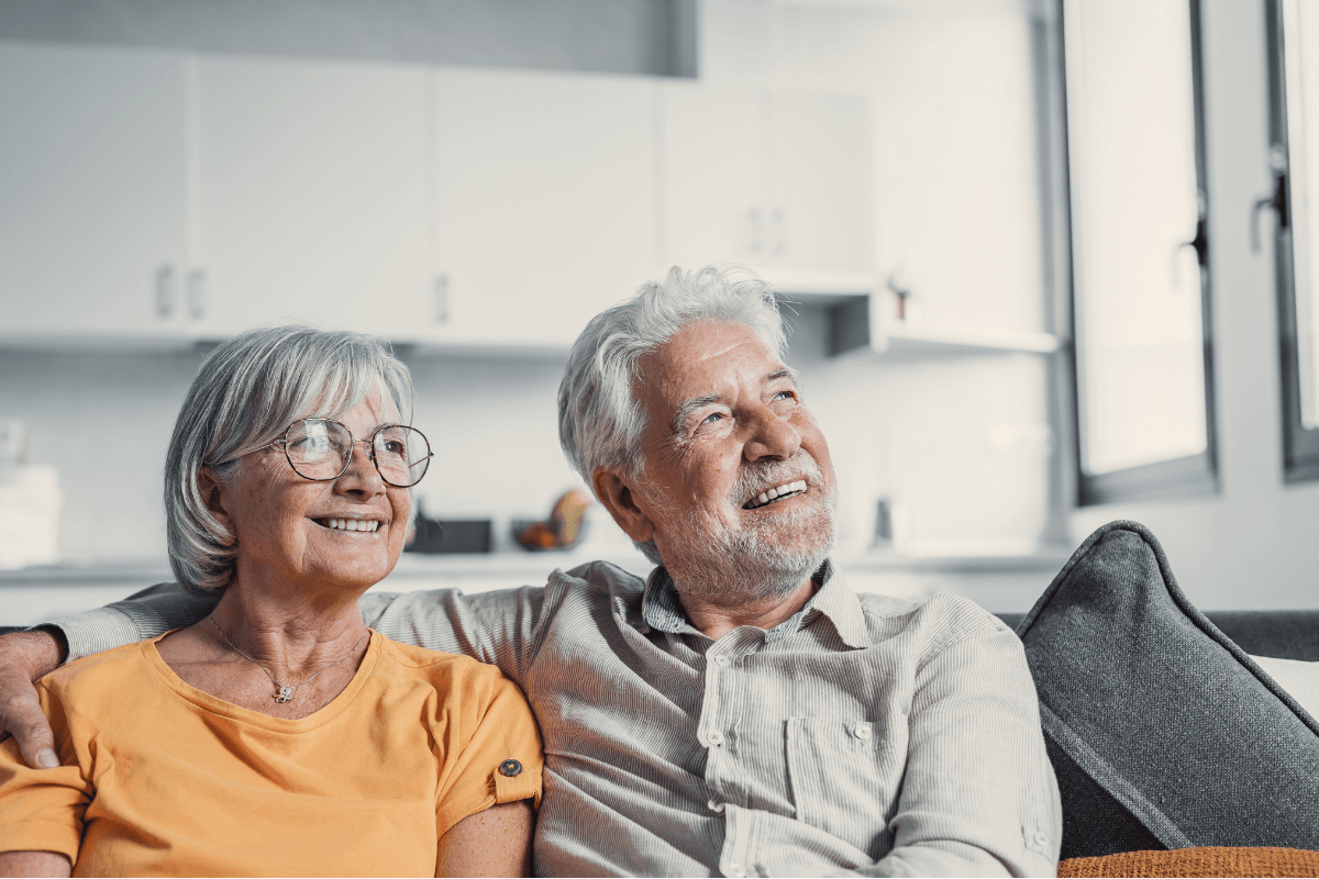 Dreamy middle aged senior loving retired family couple looking in distance, planning common future or recollecting memories, enjoying peaceful moment relaxing together on cozy sofa in living room.